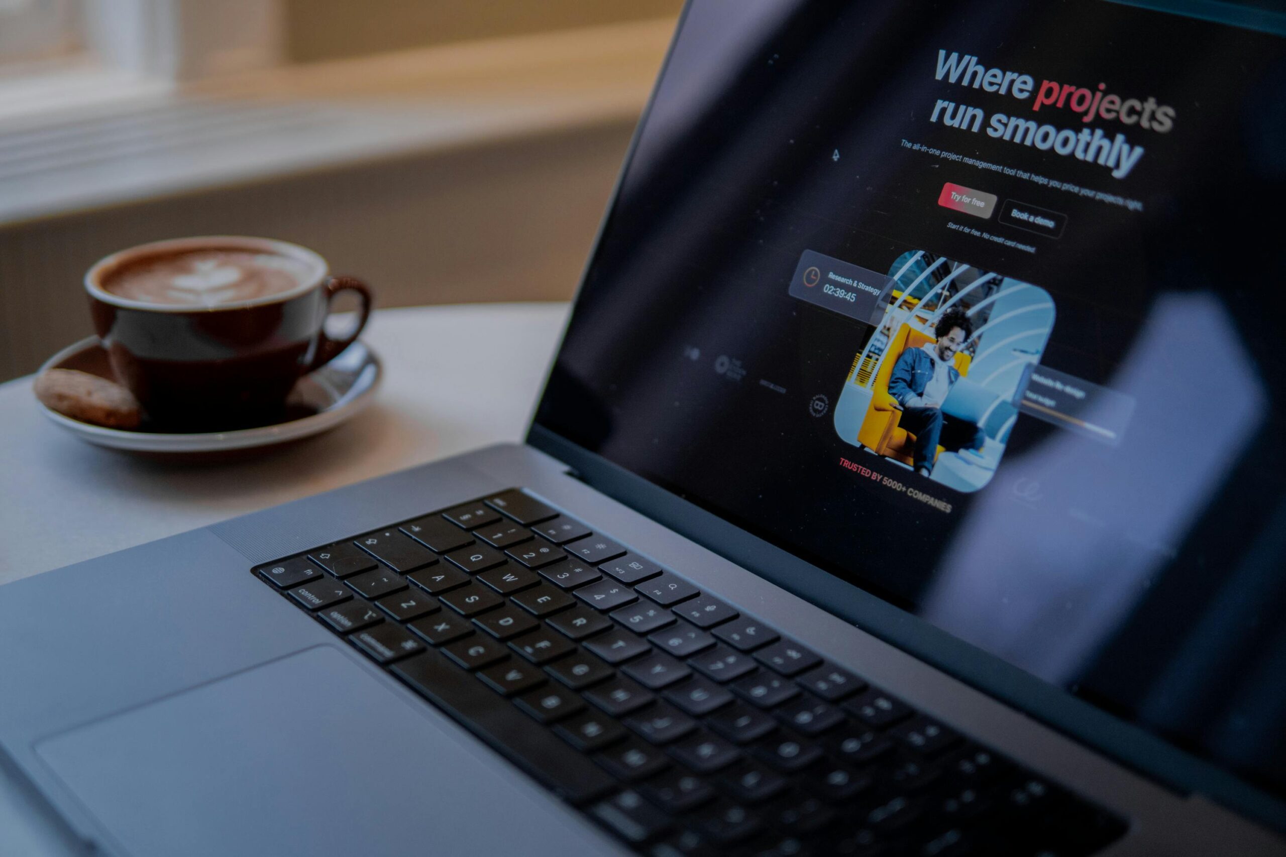 A laptop displaying a project management app sits on a table with a cozy cup of cappuccino in Amsterdam.