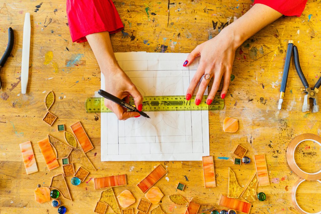 Hands crafting with colored glass on a wooden workbench, detailed top view.