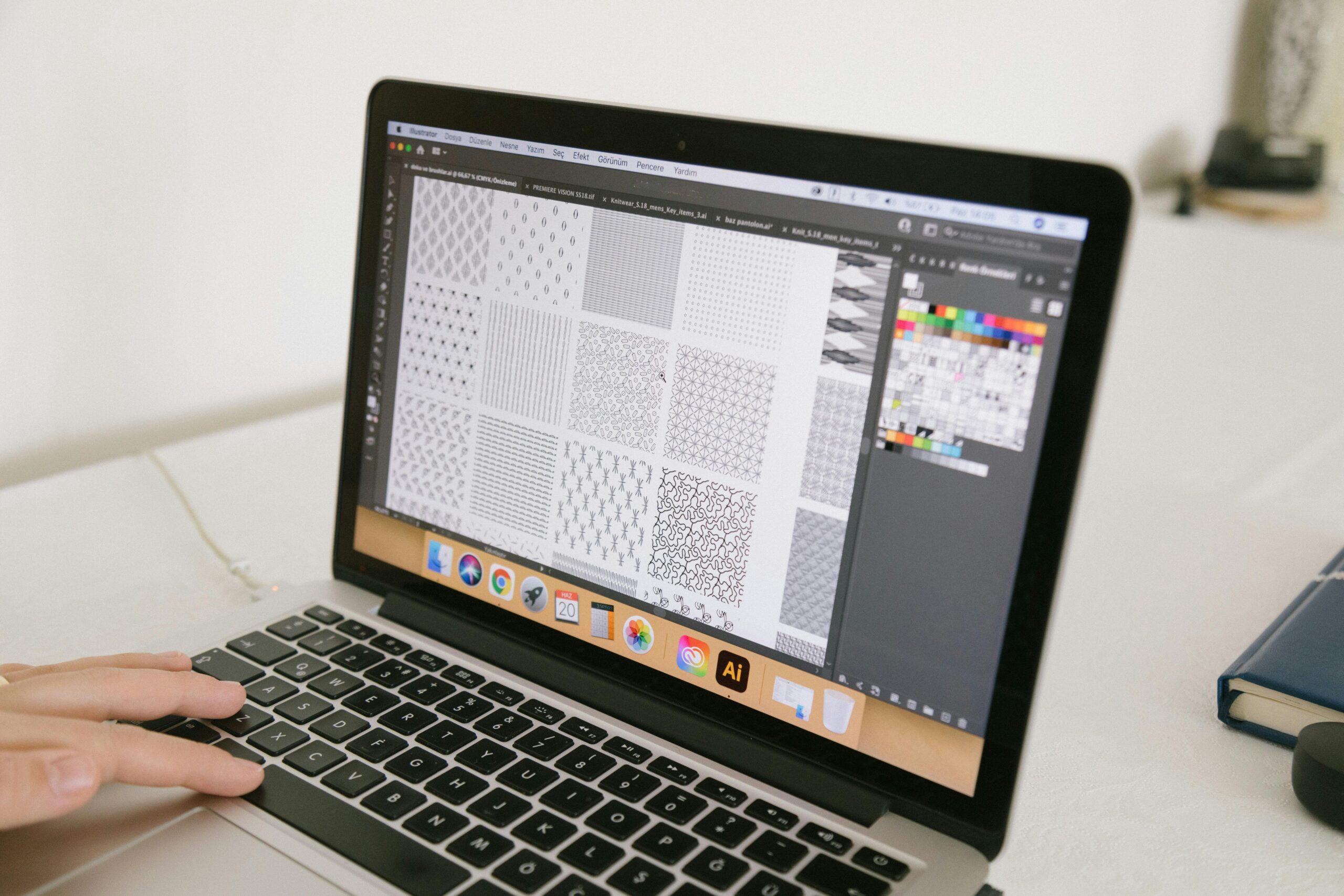 A laptop displaying graphic design patterns with a hand interacting, ideal for creative workspace themes.